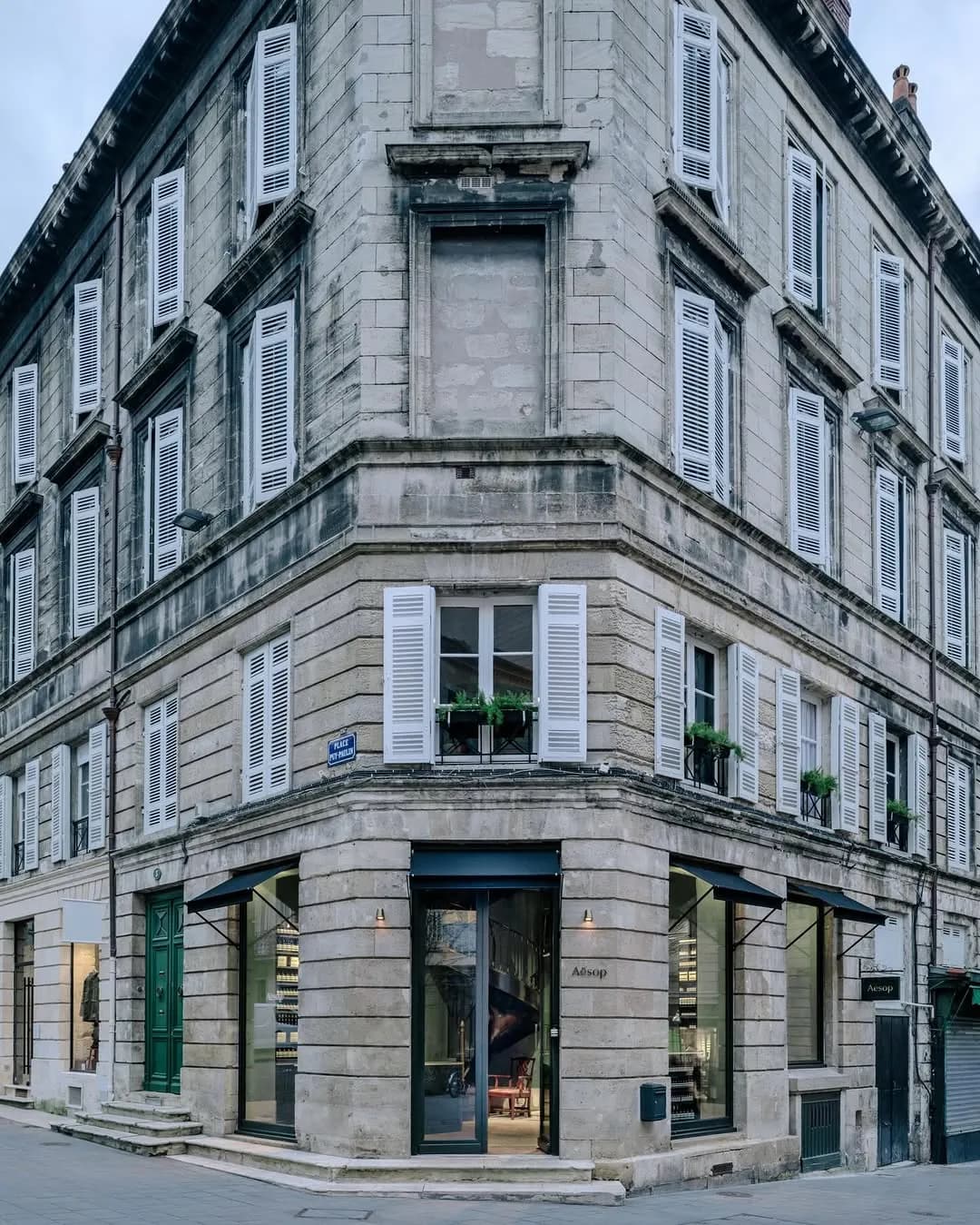 Aesop Bordeaux: evergreen depths, golden memories.
This French store, designed in-house, occupies a stately corner building on a tranquil square, seeking to recapture the original spirit of the space. Original timber parquet was discovered underneath tiles and restored—some imperfections preserved as markers of faded glory—while the gold-veined marble added to counters heightens the warmth of the velvety clay walls. The cabinetry’s rough grain emerges through pine-green paint, tracing years gone by.